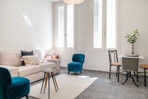 A living room with a sofa, a blue chair, a small round table, and a potted plant. - Bill – License to Thrill in Metaxourgeio (Athens)