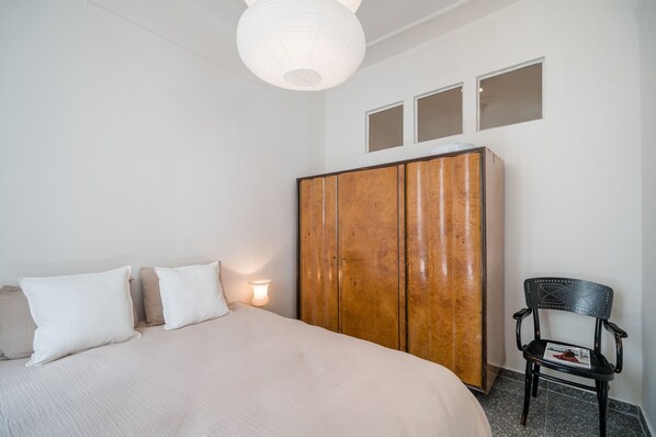 A bedroom with a bed, a wooden wardrobe, a chair, and a wall-mounted light fixture.