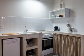 Une cuisine compacte équipée d’un lave-vaisselle, d’une cuisinière et d’un four, d’un évier et d’une étagère pour ranger les ustensiles de cuisine.