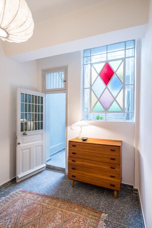 Un couloir avec une commode en bois, un tapis à motifs et une fenêtre à vitraux.