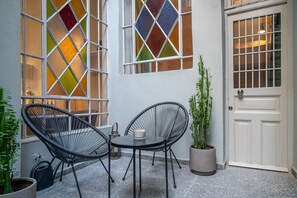 Un petit espace patio avec deux chaises en osier noir, une table ronde et une plante en pot.