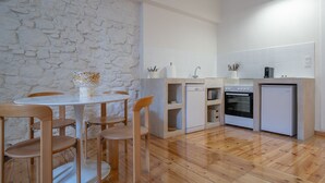 Una cocina compacta con pared de piedra, baldosas blancas, sillas de madera, una mesa de comedor, lavavajillas, horno y refrigerador.