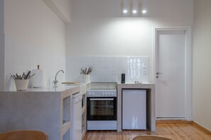 A compact kitchen with white tiles, a built-in oven, a small refrigerator, and a wooden floor.