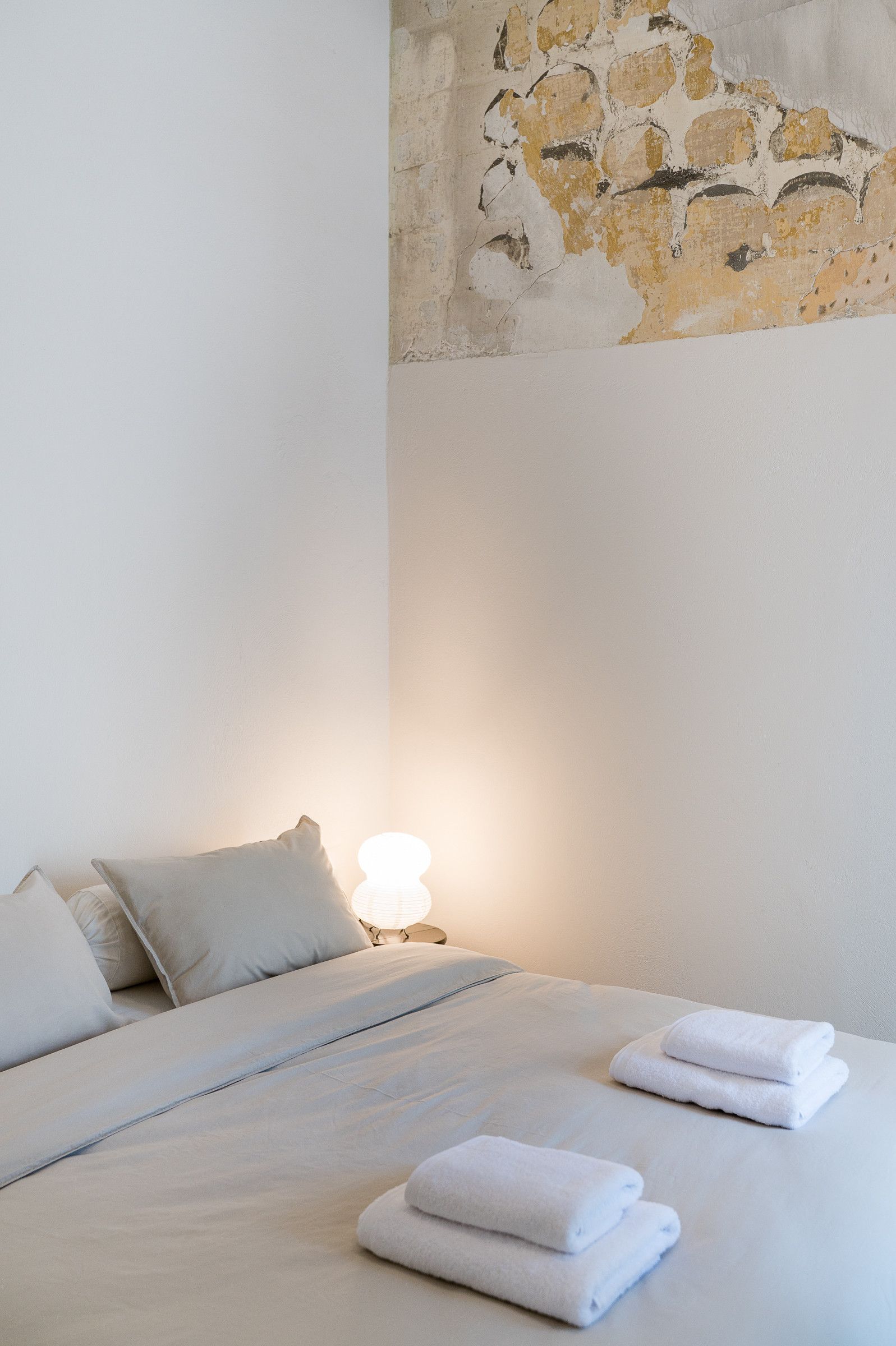 Habitación de hotel con cama, almohadas, una lámpara y una pared con textura de piedra.