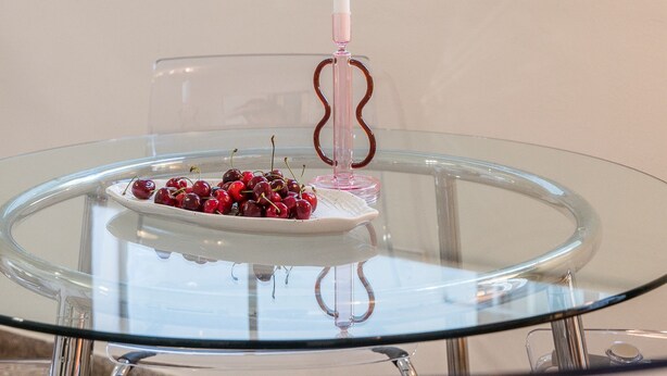 A glass table with a white candle and a plate of cherries. - Charlie – Timeless Charm & Modern Comfort (Athens)