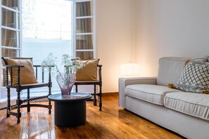 A living room with a wooden floor, a round coffee table, two armchairs, a sofa, and a window with curtains. - Charlie – Timeless Charm & Modern Comfort (Athens)