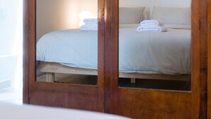 A wooden wardrobe with mirrored doors, a bed with white linens, and a lamp on top. - Charlie – Timeless Charm & Modern Comfort (Athens)