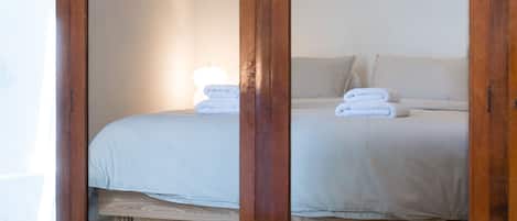 A wooden wardrobe with mirrored doors, a bed with white linens, and a lamp on top.
