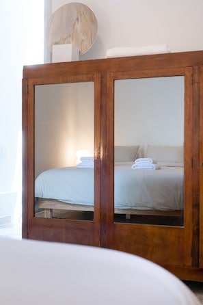 A wooden wardrobe with mirrored doors, a bed with white linens, and a lamp on top. - Charlie – Timeless Charm & Modern Comfort (Athens)