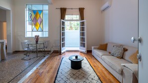 A modern living room with a glass dining table, a sofa, and a large window with curtains. - Charlie – Timeless Charm & Modern Comfort (Athens)