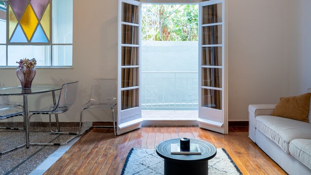 A room with a glass table, chairs, a sofa, a coffee table, and a large window with curtains. - Charlie – Timeless Charm & Modern Comfort (Athens)