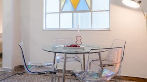 A dining area with a glass table and chairs, a candle, and a stained glass window. - Charlie – Timeless Charm & Modern Comfort (Athens)
