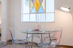 A dining area with a glass table and chairs, a candle, and a stained glass window. - Charlie – Timeless Charm & Modern Comfort (Athens)