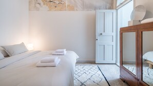 A bedroom with a bed, a wooden nightstand, a white door, and a stone wall. - Charlie – Timeless Charm & Modern Comfort (Athens)
