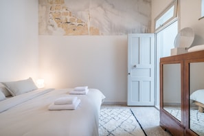 A bedroom with a bed, a wooden nightstand, a white door, and a stone wall. - Charlie – Timeless Charm & Modern Comfort (Athens)
