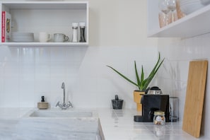 A kitchen with a marble sink, a coffee machine, a plant, and a shelf with kitchenware. - Charlie – Timeless Charm & Modern Comfort (Athens)
