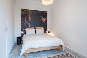A bedroom with a bed, a wall-mounted artwork, a bedside lamp, and a rug. - Crane – Stylish Living in the Heart of Metaxourgeio (Athens)
