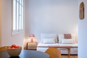 A minimalist living room with a sofa, a table, and a lamp. - Crane – Stylish Living in the Heart of Metaxourgeio (Athens)