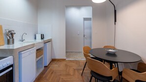 Une cuisine compacte dotée d’appareils électroménagers modernes, un coin repas avec une table ronde et des chaises, et un couloir menant à une porte.