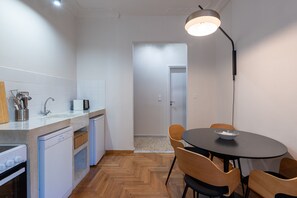 Une cuisine compacte dotée d’appareils électroménagers modernes, un coin repas avec une table ronde et des chaises, et un couloir menant à une porte.
