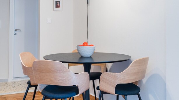 Un coin repas avec une table ronde, quatre chaises, un saladier de fruits et un luminaire suspendu moderne.