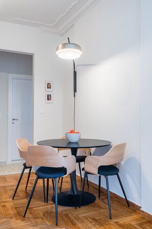 Ruokailutila, jossa on pyöreä pöytä, neljä tuolia, hedelmäkulho ja moderni riippuvalaisin.