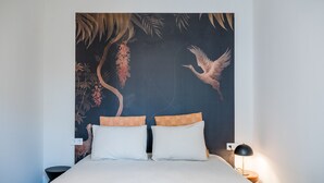 Un lit avec deux oreillers, une table de chevet avec une lampe et un mur orné d’une fresque aux motifs tropicaux.