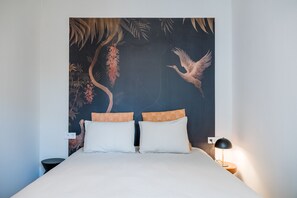 Un lit avec deux oreillers, une table de chevet avec une lampe et un mur orné d’une fresque aux motifs tropicaux.
