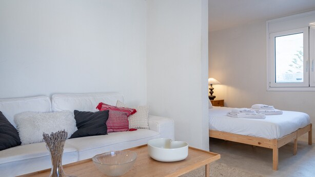 A minimalist bedroom with a wooden bed, a white bedside table, and a white sofa with cushions. - Astrid – A Serene Rooftop Escape in Athens (Athens)
