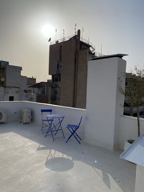 Una terraza en la azotea con una pared blanca, una silla plegable azul y una mesa.