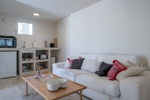 A modern living room with a white sofa, a wooden coffee table, and a kitchen area with white cabinets and a microwave. - Astrid – A Serene Rooftop Escape in Athens (Athens)