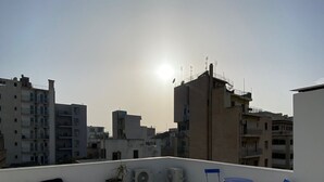 A rooftop terrace with a clear view of the city skyline, a few potted plants, and blue folding chairs. - Astrid – A Serene Rooftop Escape in Athens (Athens)