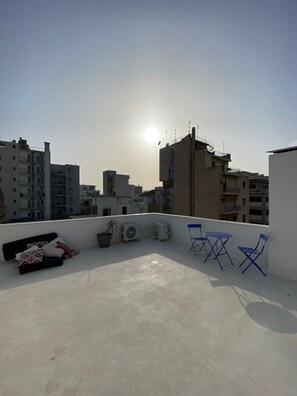 A rooftop terrace with a clear view of the city skyline, a few potted plants, and blue folding chairs. - Astrid – A Serene Rooftop Escape in Athens (Athens)