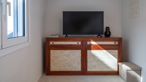 A room with a television on a wooden cabinet, a small bench, and a window with blinds. - Astrid – A Serene Rooftop Escape in Athens (Athens)
