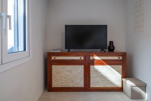 A room with a television on a wooden cabinet, a small bench, and a window with blinds. - Astrid – A Serene Rooftop Escape in Athens (Athens)
