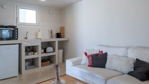 A modern kitchen with a built-in microwave, toaster, and sink. There is a white sofa with cushions and a vase with dried flowers on a wooden table. - Astrid – A Serene Rooftop Escape in Athens (Athens)