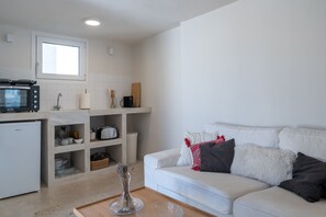 A modern kitchen with a built-in microwave, toaster, and sink. There is a white sofa with cushions and a vase with dried flowers on a wooden table. - Astrid – A Serene Rooftop Escape in Athens (Athens)