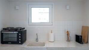 A kitchen with a built-in oven, a sink, a window, and a wooden cutting board. - Astrid – A Serene Rooftop Escape in Athens (Athens)