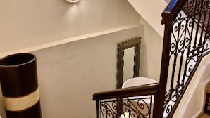 Uma escadaria com corrimão de ferro forjado, um luminário fixado na parede e um espelho.