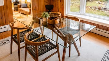 A dining area with a glass table and wooden chairs, a potted plant, and a view of the outdoors.