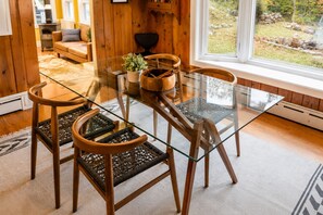 Comedor con mesa de vidrio, sillas de madera, una planta en maceta y vista al exterior.