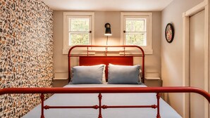 Una cama con estructura metálica roja, dos almohadas y una pared con estampado floral.