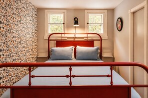 Un lit avec un cadre en métal rouge, deux oreillers et un mur orné d’un motif floral.