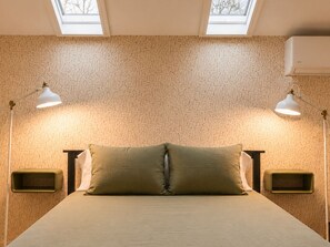 Ein Zimmer mit einem Bett, zwei Nachttischen, einem Oberlicht und einer Wand-Klimaanlage.