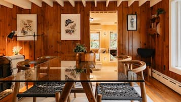 Een kamer met houten lambrisering, een glazen eettafel, gevlochten stoelen en ingelijste kunstwerken aan de wanden.