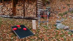 Un espace extérieur comprenant une table noire, des coussins rouges, une structure en bois où est entreposé du bois de chauffage, et une structure métallique pour l’escalade.