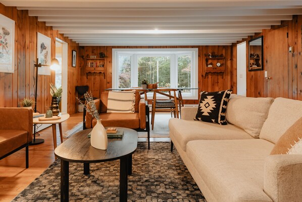 A cozy living room with wooden walls, a sofa, a coffee table, and a dining area with a table and chairs.