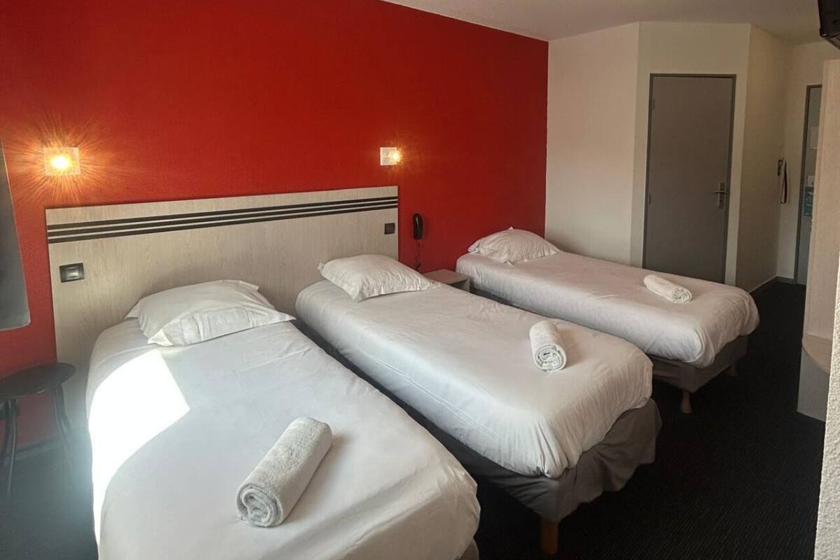 Une chambre d’hôtel avec trois lits, un mur rouge et une porte.