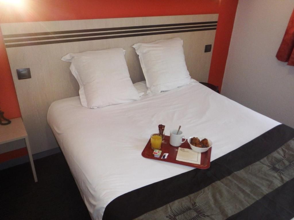 Une chambre d’hôtel avec un lit, du linge de lit blanc, un plateau avec des articles pour le petit-déjeuner et un mur rouge.