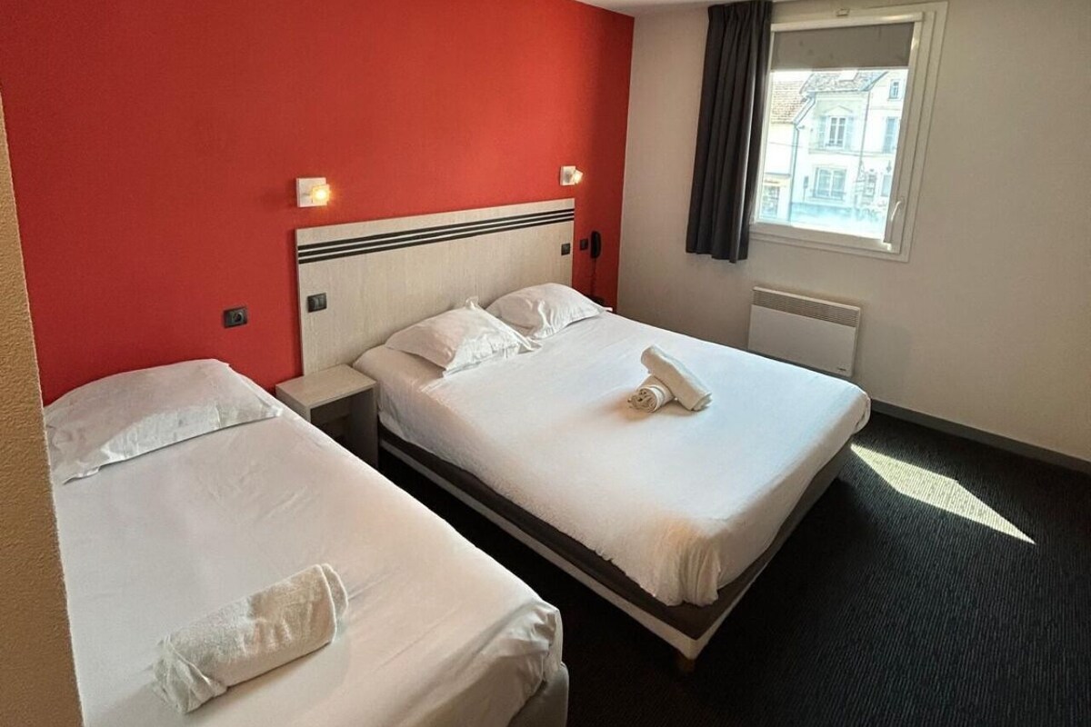 A hotel room with two beds, a red accent wall, and a window with a view.